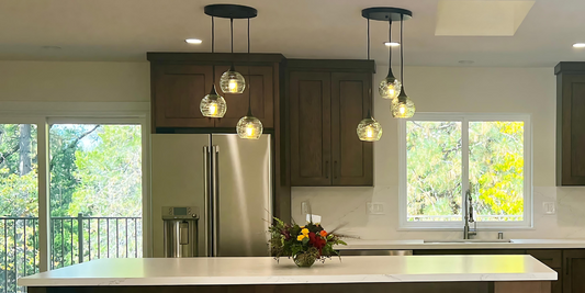 two black 3 light pendant chandeliers with clear glass globes in a white and black kitchen 