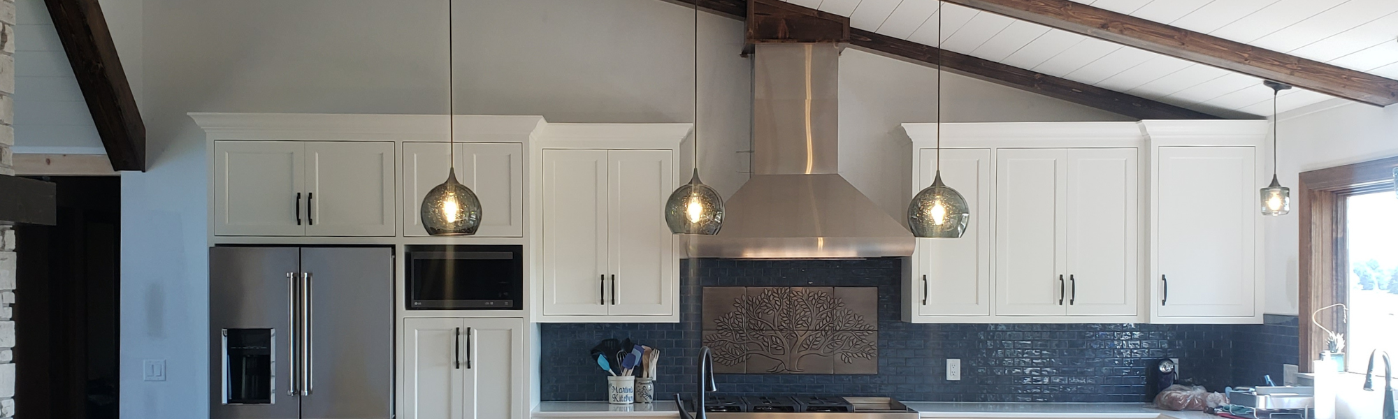 photo of kitchen with tall slanted ceiling featuring three glass pendant lights 