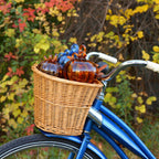 A wicker basket filled with decorative glass pumpkins on the front of a blue bicycle, set against a background of colorful autumn foliage.