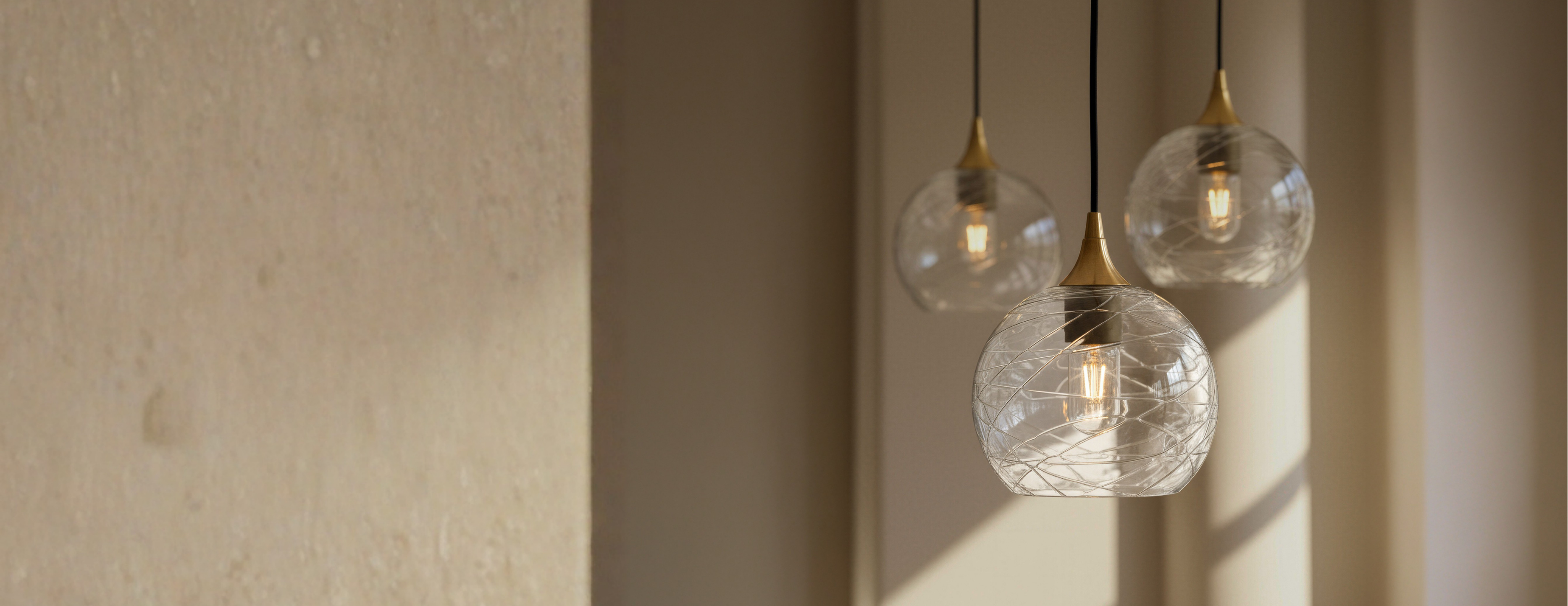 Three glass pendant lights hanging against a beige wall
