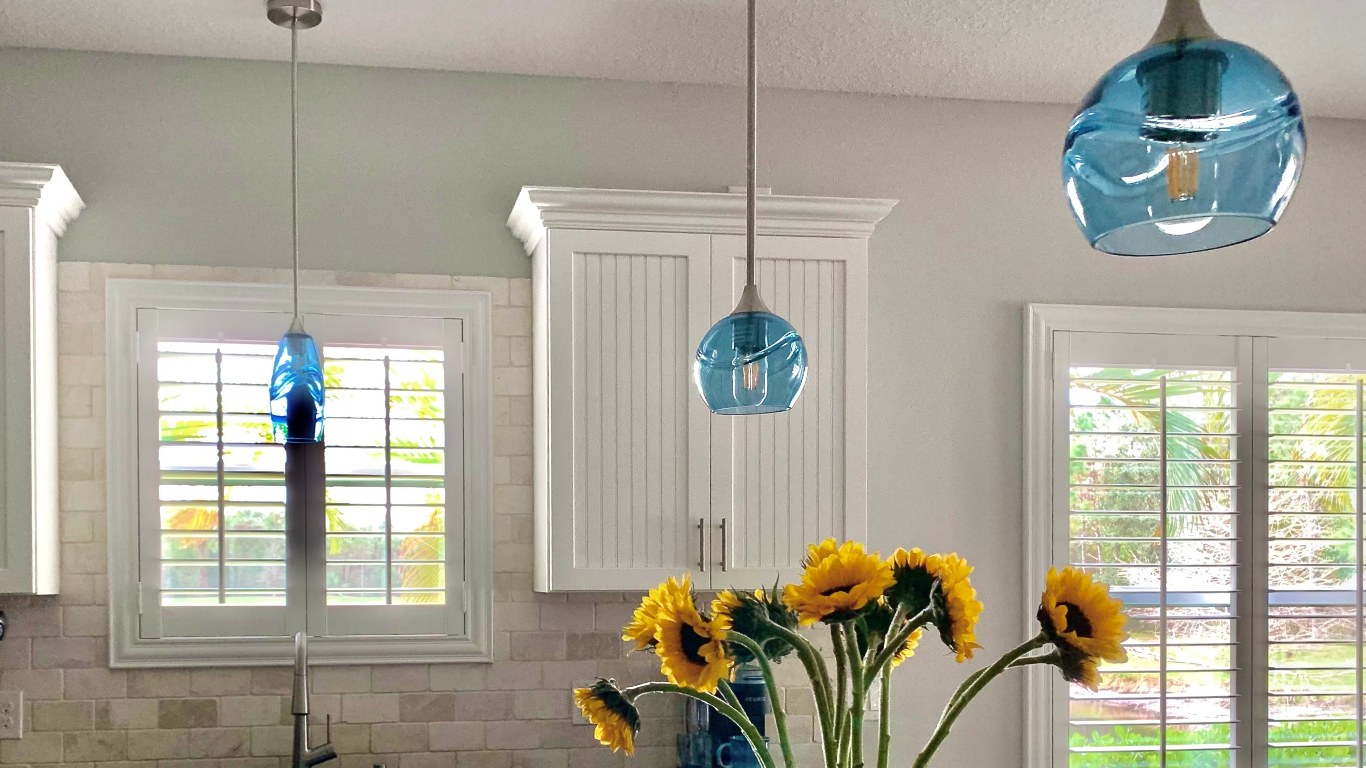 Kitchen interior with white cabinets, blue pendant lights, and yellow flowers.